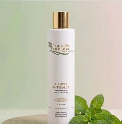Flacone di shampoo antigiallo Cannella Damiana accanto a foglie di menta